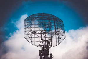 A large radar antenna, a key component of a system that relies on radar filters, silhouetted against a dynamic blue and white sky.