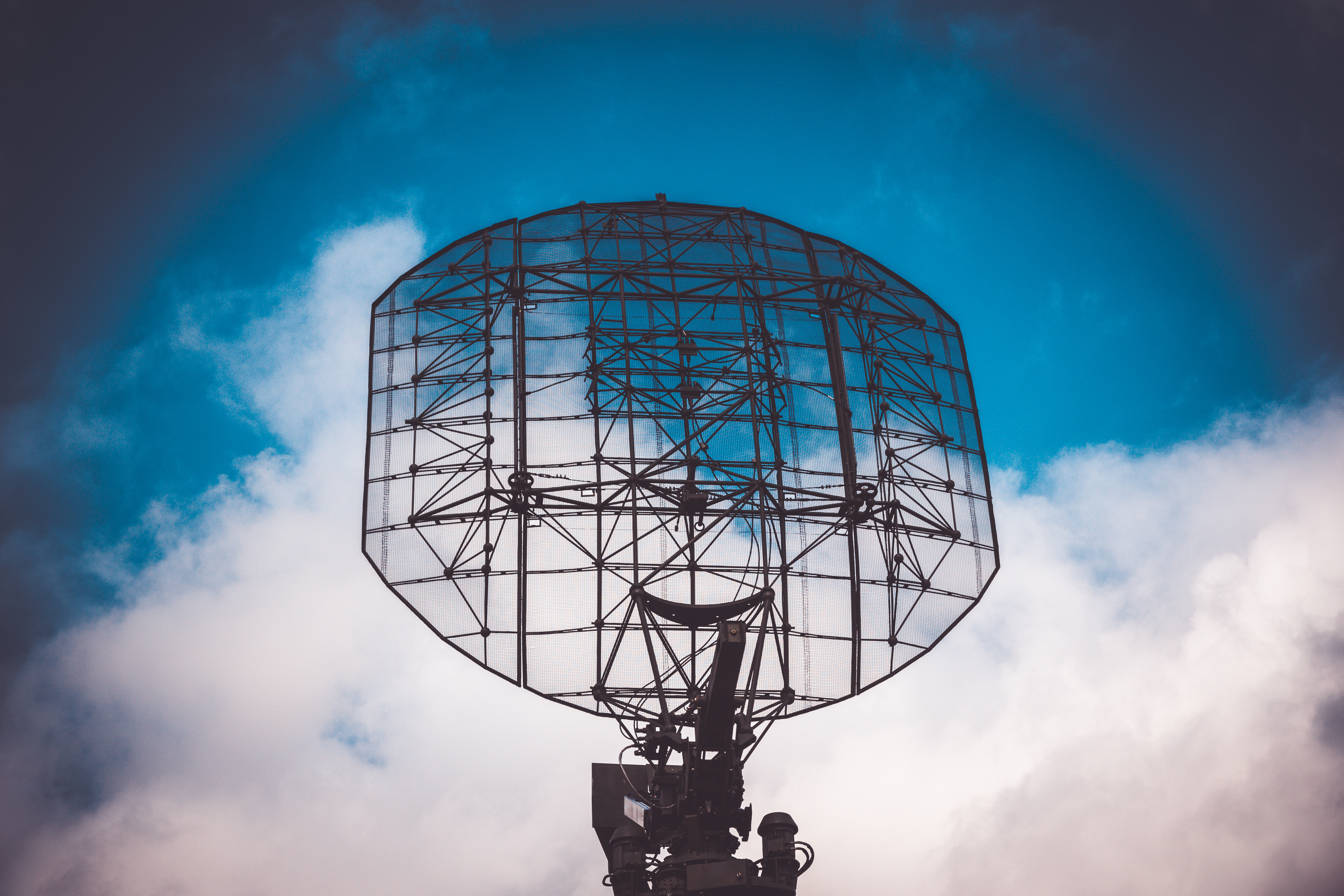A large radar antenna, a key component of a system that relies on radar filters, silhouetted against a dynamic blue and white sky.